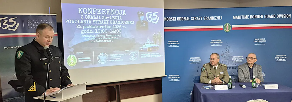 Funkcjonariusz w granatowym mundurze przemawia przy mównicy, w tle ekran z zaproszeniem na konferencję i dwaj uczestnicy przy stole