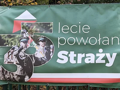 Fragment zielonego baneru z jubileuszowym logo „35” i napisem „lecie powołania Straży Granicznej”, na logo funkcjonariusze z pocztem sztandarowym
