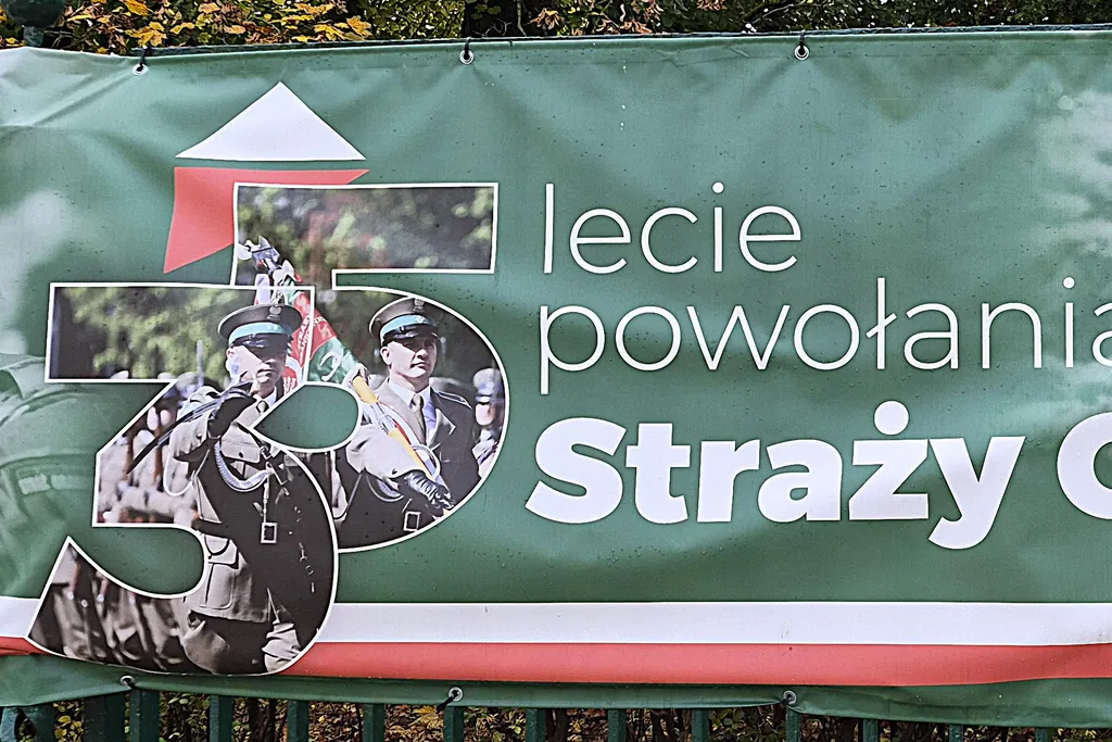 Fragment zielonego baneru z jubileuszowym logo „35” i napisem „lecie powołania Straży Granicznej”, na logo funkcjonariusze z pocztem sztandarowym