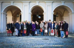 Grupa dyplomatów i ich bliskich pozuje na dziedzińcu przed jasną, arkadową fasadą pałacu
