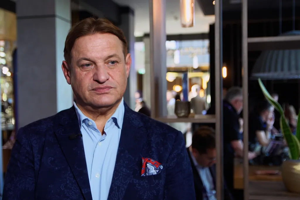 Prof. Jacek Męcina w granatowej marynarce i błękitnej koszuli, w tle wnętrze kawiarni