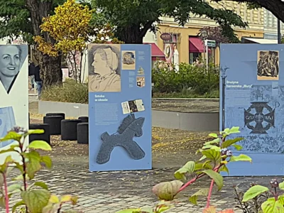 Rząd plenerowych plansz wystawy IPN na szczecińskim placu Zgody: portrety kobiet, plansza „Sztuka w obozie”, plansza o drużynie harcerskiej „Mury”, plansze o pracy przymusowej i obozowych barakach