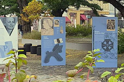 Rząd plenerowych plansz wystawy IPN na szczecińskim placu Zgody: portrety kobiet, plansza „Sztuka w obozie”, plansza o drużynie harcerskiej „Mury”, plansze o pracy przymusowej i obozowych barakach