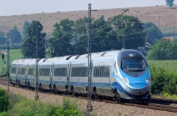 Biało-niebieski pociąg Pendolino PKP Intercity jedzie po torach wśród drzew i pól