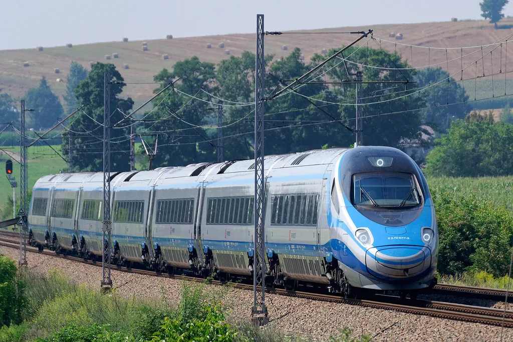 Biało-niebieski pociąg Pendolino PKP Intercity jedzie po torach wśród drzew i pól